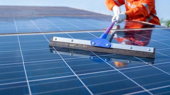 Technician cleaning solar panels with a soft squeegee